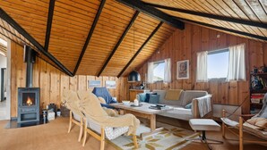 A cozy cabin interior with a wood-burning stove, a sofa, a chair, and a dining table.