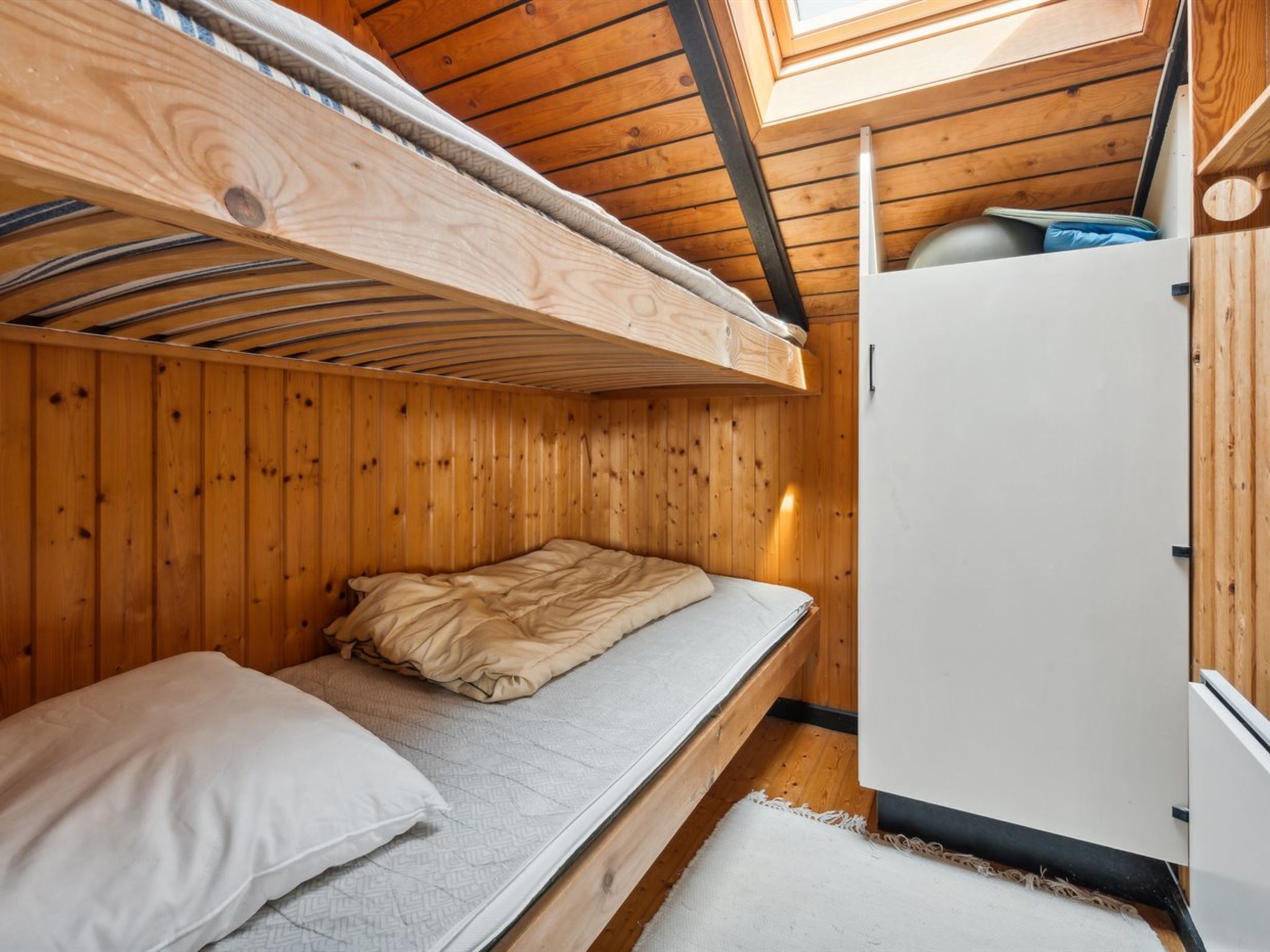 A compact wooden cabin with a bunk bed, a small white refrigerator, and a skylight.