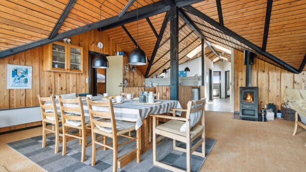 A cozy wooden cabin with a dining area featuring a table and chairs, a kitchen with cabinets, and a fireplace.