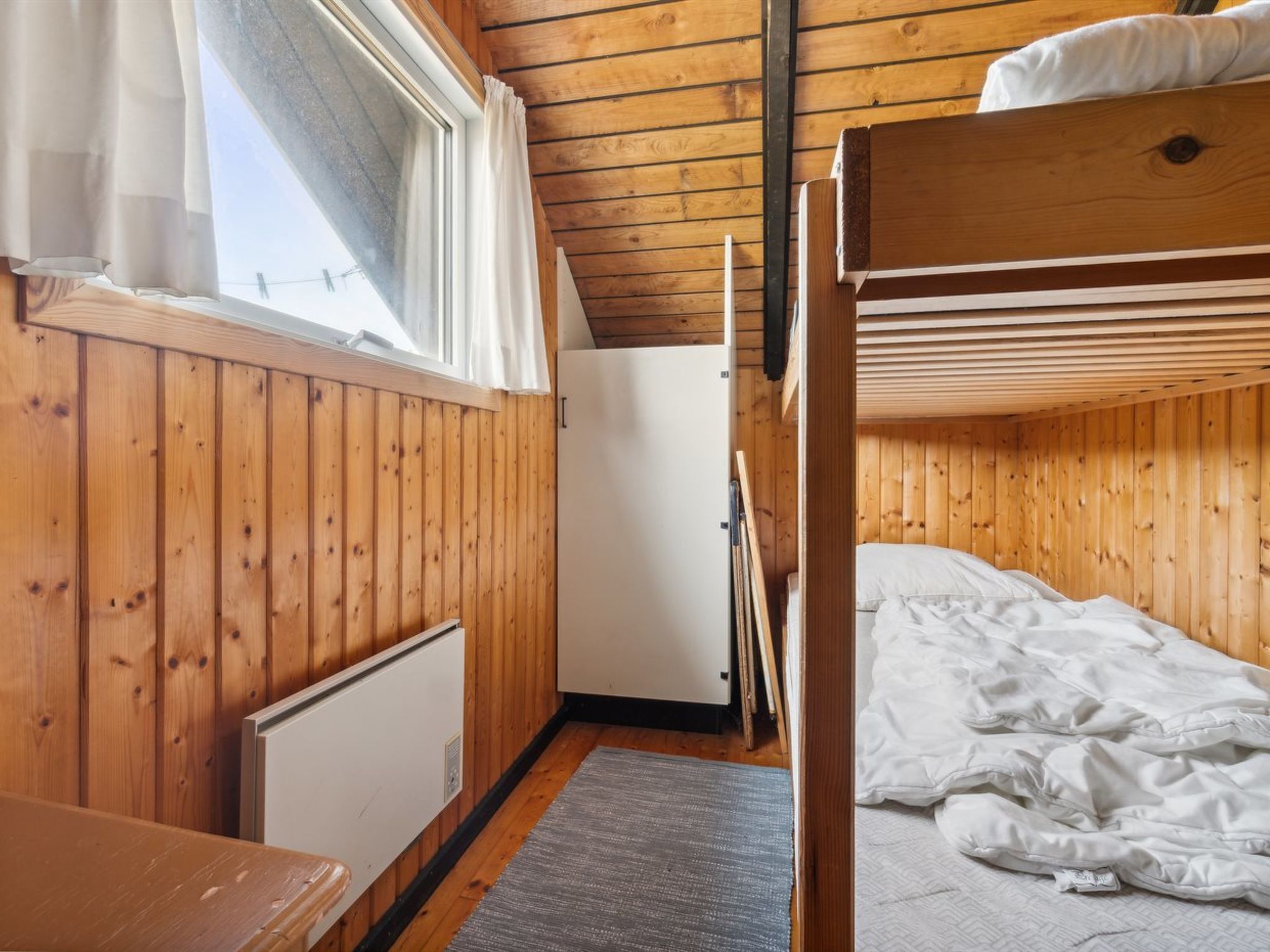 Ein Zimmer mit Holzboden, Etagenbetten, einem Heizkörper und einem Fenster mit Vorhängen.