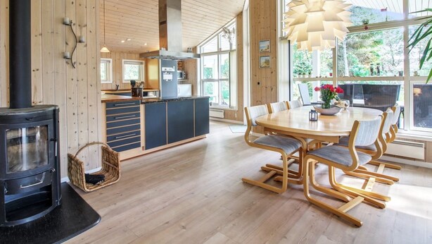 A modern kitchen with wooden cabinetry, a central island, and a dining area with a round table and chairs. - "Arlett" - 950m from the sea by Interhome (Fjerritslev)