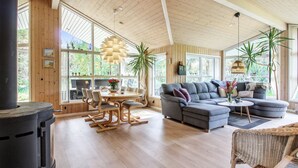 A spacious living area with a large wooden ceiling, a fireplace, a grey sofa, and a dining table with chairs. - "Arlett" - 950m from the sea by Interhome (Fjerritslev)