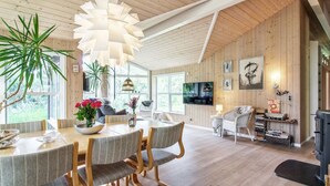 A spacious living area with a wooden ceiling, a dining table with chairs, a television, and a fireplace. - "Arlett" - 950m from the sea by Interhome (Fjerritslev)