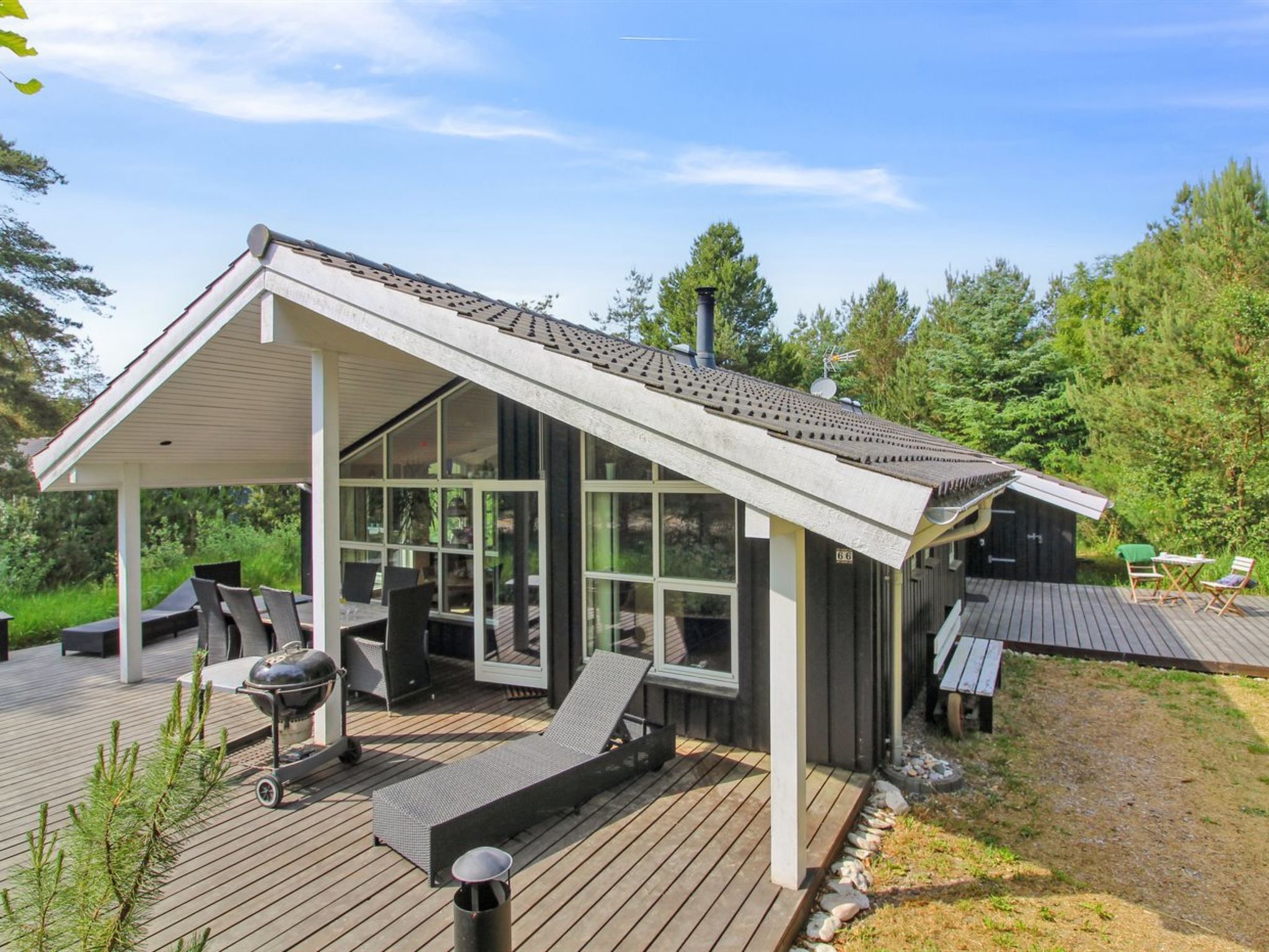 A modern outdoor deck with a covered seating area, a grill, and a small shed.