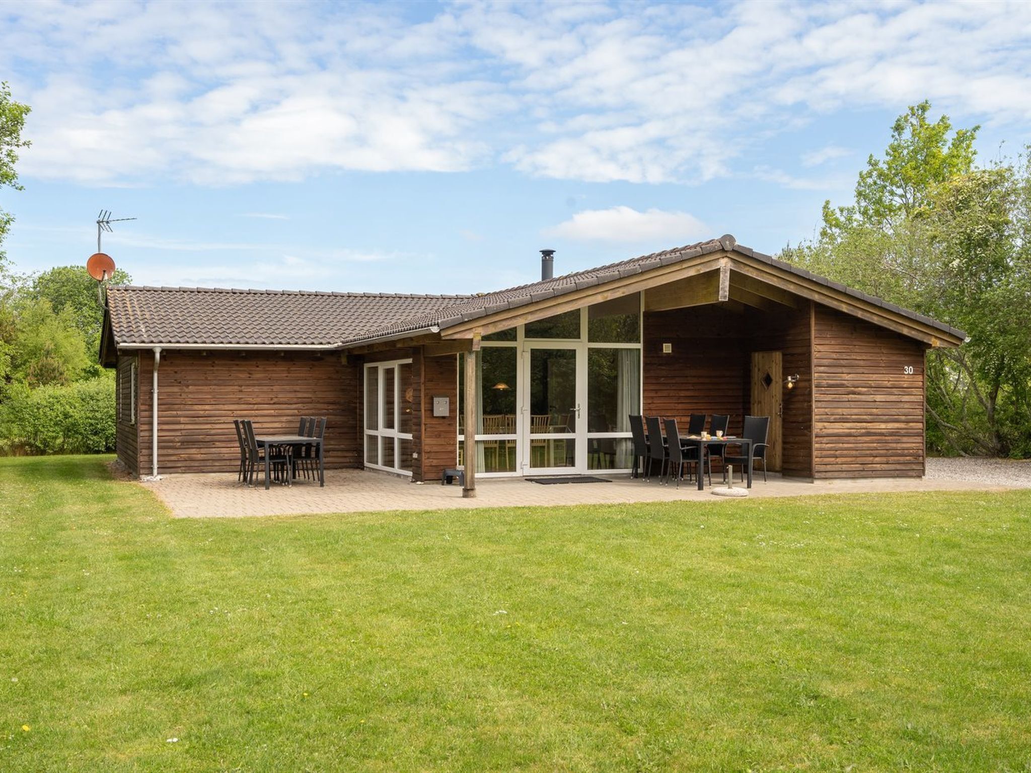 A wooden cabin with a tiled roof, large glass doors, and a patio area with outdoor seating.