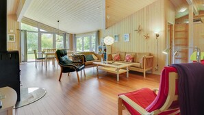 Een ruime woonkamer met houten vloeren, een zithoek, een eettafel en een glazen salontafel.