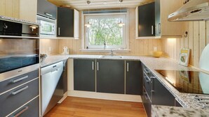 Een moderne keuken met houten kastjes, een inbouwoven en een raam dat voor natuurlijk licht zorgt.