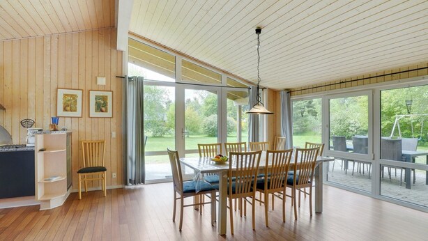 Een moderne keuken met houten kastjes, een eethoek met tafel en stoelen, en grote ramen met uitzicht op het omliggende landschap.