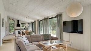 Ein modernes Wohnzimmer mit einer Eckcouch, einem Glastisch und einem an der Wand montierten Fernseher.
