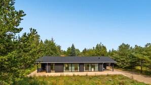 Ein modernes Haus mit Flachdach, großen Fenstern und einer überdachten Terrasse.