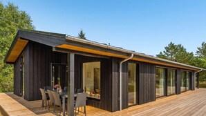 Ein modernes Gebäude mit einer Holterrasse, großen Fenstern und einer überdachten Außenbereich-Sitzgelegenheit.
