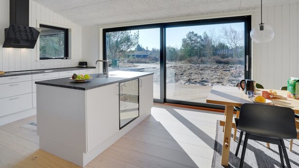 Eine moderne Küche mit einer großen Kochinsel, einem Essbereich mit Tisch und Stühlen sowie Blick auf eine angelegte Außenanlage.