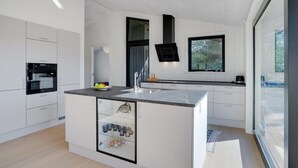 Eine moderne Küche mit weißen Schränken, einer zentralen Kochinsel mit Spüle und einem integrierten Weinkühlschrank.