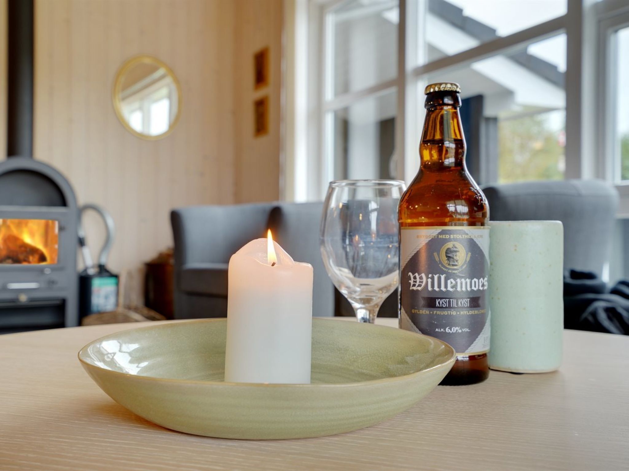A cozy room with a fireplace, a candle, a bottle of Willemoos KYST til KYST beer, and a glass.