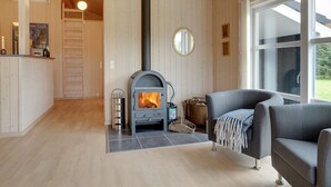 A cozy living room with a wood-burning stove, a comfortable gray sofa, and a large window providing a view of the outdoors. - "Frida" - 700m from the sea by Interhome (Fjerritslev)
