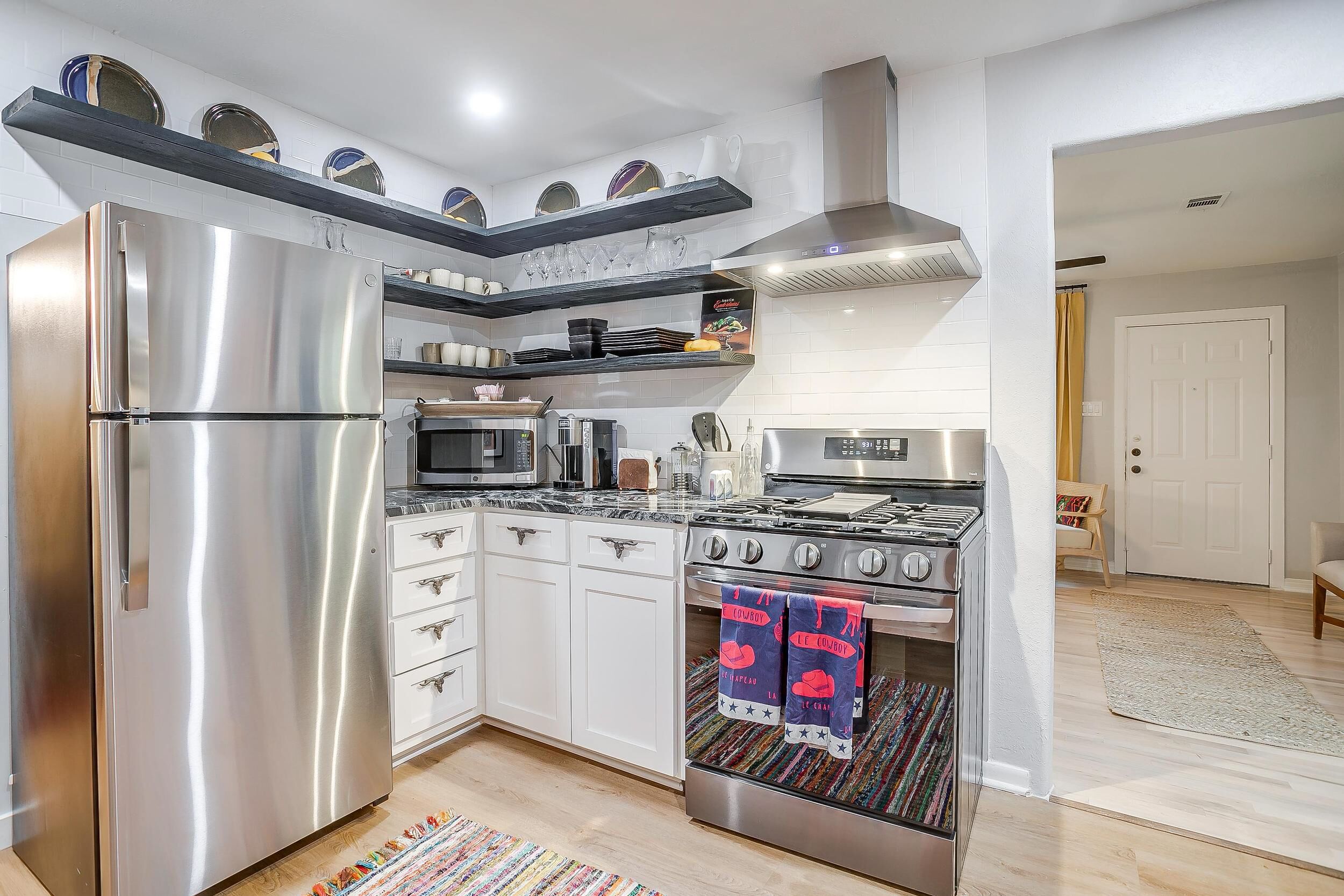 A modern kitchen with stainless steel appliances, white cabinetry, and a patterned rug.
