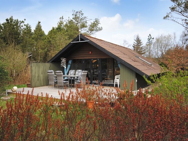 Une cabane avec un toit en pente, une terrasse dotée de mobilier d’extérieur et une vue sur la forêt environnante.