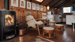 Interior acolhedor de cabana com lareira a lenha, área de jantar com mesa e cadeiras, cozinha equipada e obras de arte emolduradas nas paredes.