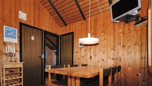 Interior de madeira com mesa de jantar, cadeiras, adega e televisão fixada na parede.