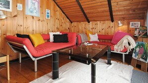 Interior acolhedor de uma cabana com teto de madeira, um sofá vermelho, uma mesa de centro de vidro e uma pequena estante.