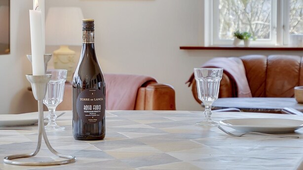 A dining table with a bottle of rosso fudco wine, a lit candle, and two wine glasses.
