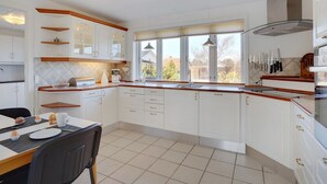 A modern kitchen with white cabinets, a dining area with a table and chairs, and a large window providing natural light.