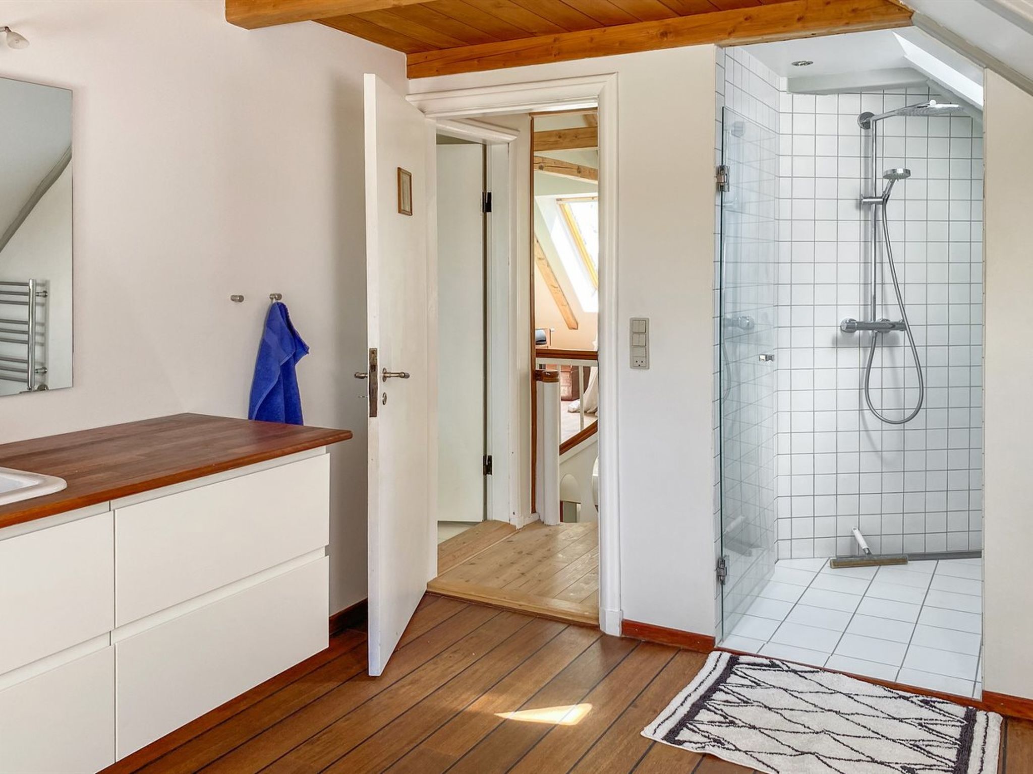 A modern bathroom with a wooden vanity, a glass shower enclosure, and a visible skylight.