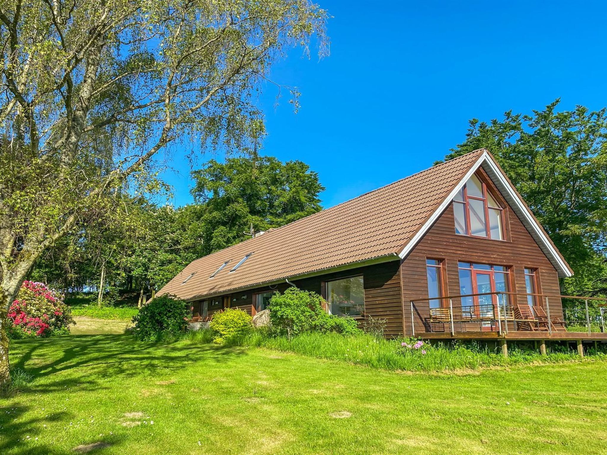 Une cabane en bois avec un toit en pente, de grandes fenêtres et une véranda dotée de sièges d’extérieur.