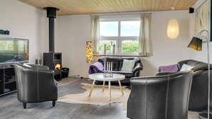 Ein modernes Wohnzimmer mit Kamin, Ledersofas, Fernseher und einem großen Fenster mit Vorhängen.