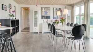 Ein moderner Essbereich mit einem langen Tisch und schwarzen Stühlen, einem weißen Schrank mit Glastüren und einer Holzzahl.