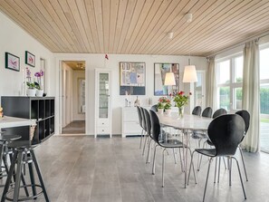 Ein moderner Essbereich mit einem langen Tisch und schwarzen Stühlen, einem weißen Schrank mit Glastüren und einer Holzzahl.