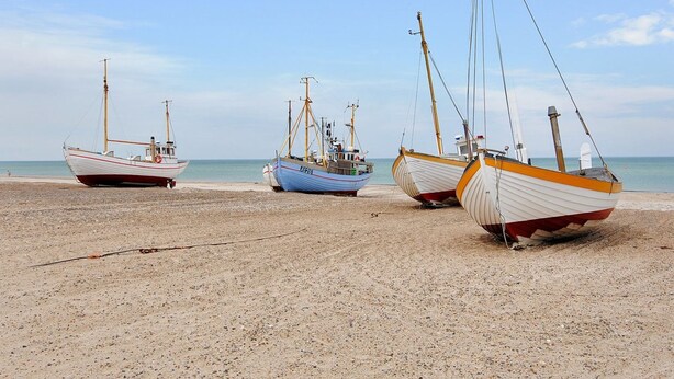 Trois bateaux sur une plage de sable, avec la mer en arrière-plan.
