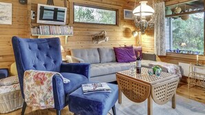 Interior acogedor de una cabaña con un sillón azul, un sofá, una pequeña mesa de madera y un televisor en la pared.