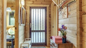 Interior de madera con una puerta, una mesita con una lámpara, una silla, un aparador y un jarrón con flores.