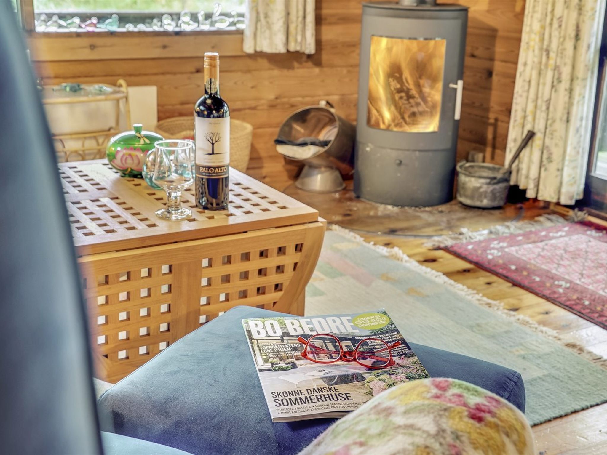 L’intérieur chaleureux d’un chalet avec une table en bois, une bouteille de vin, des verres et un magazine.