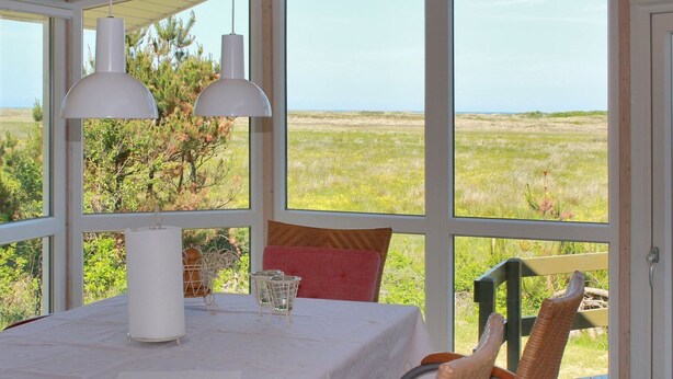 A dining area with a table set for two, two pendant lights, and a view of a grassy field through large windows.