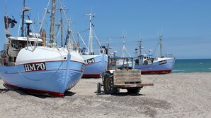 Three fishing boats with visible hull numbers HM70, HM92, and HM84 docked on a sandy beach.