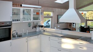A modern kitchen with white cabinets, a built-in oven, a dishwasher, and a large window providing natural light.
