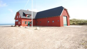 En röd byggnad med ett sluttande tak, en flaggstång och en sandstrand i bakgrunden.