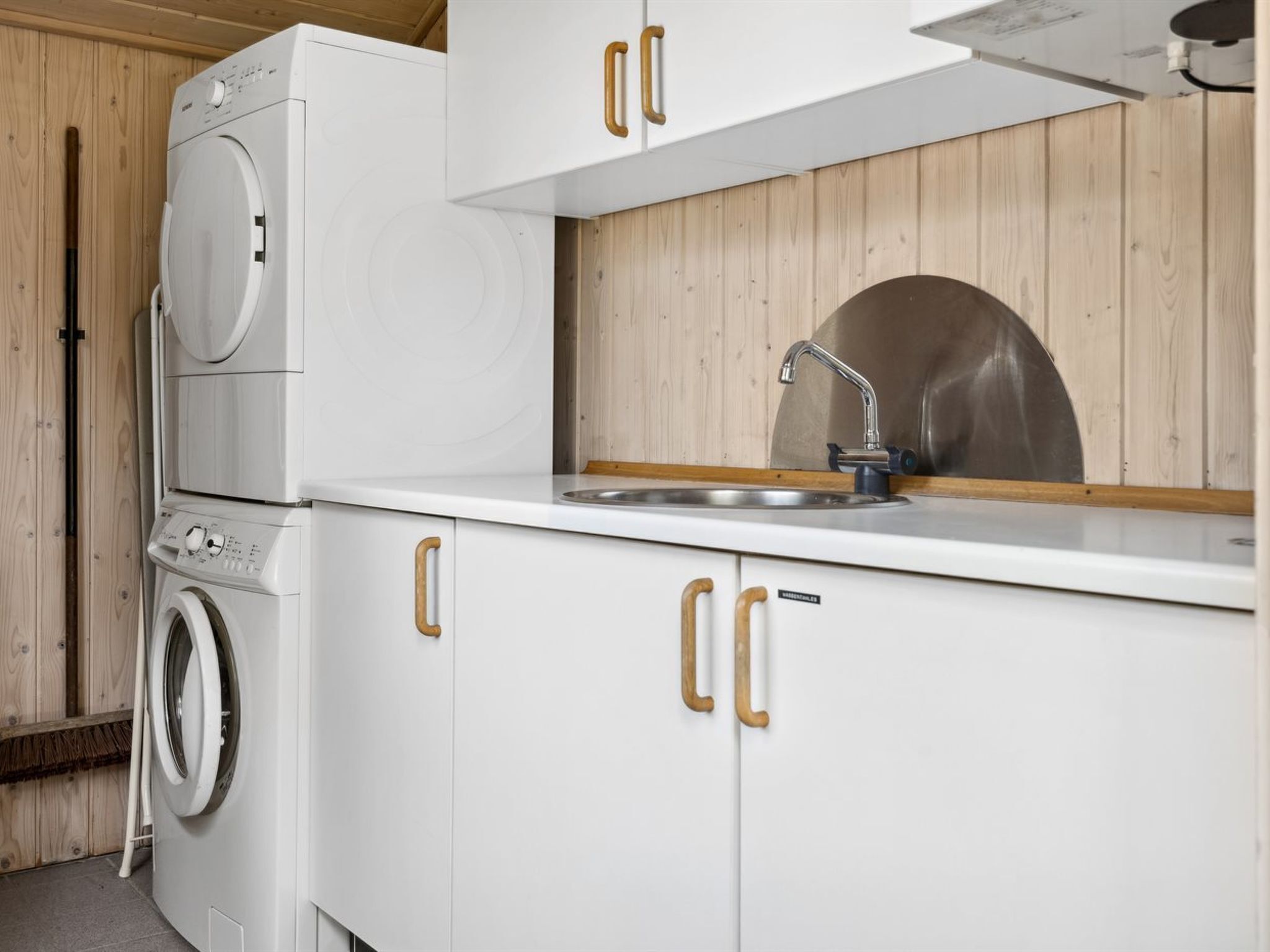 Een kleine keuken met een wasmachine, een spoelbak en houten kastjes.