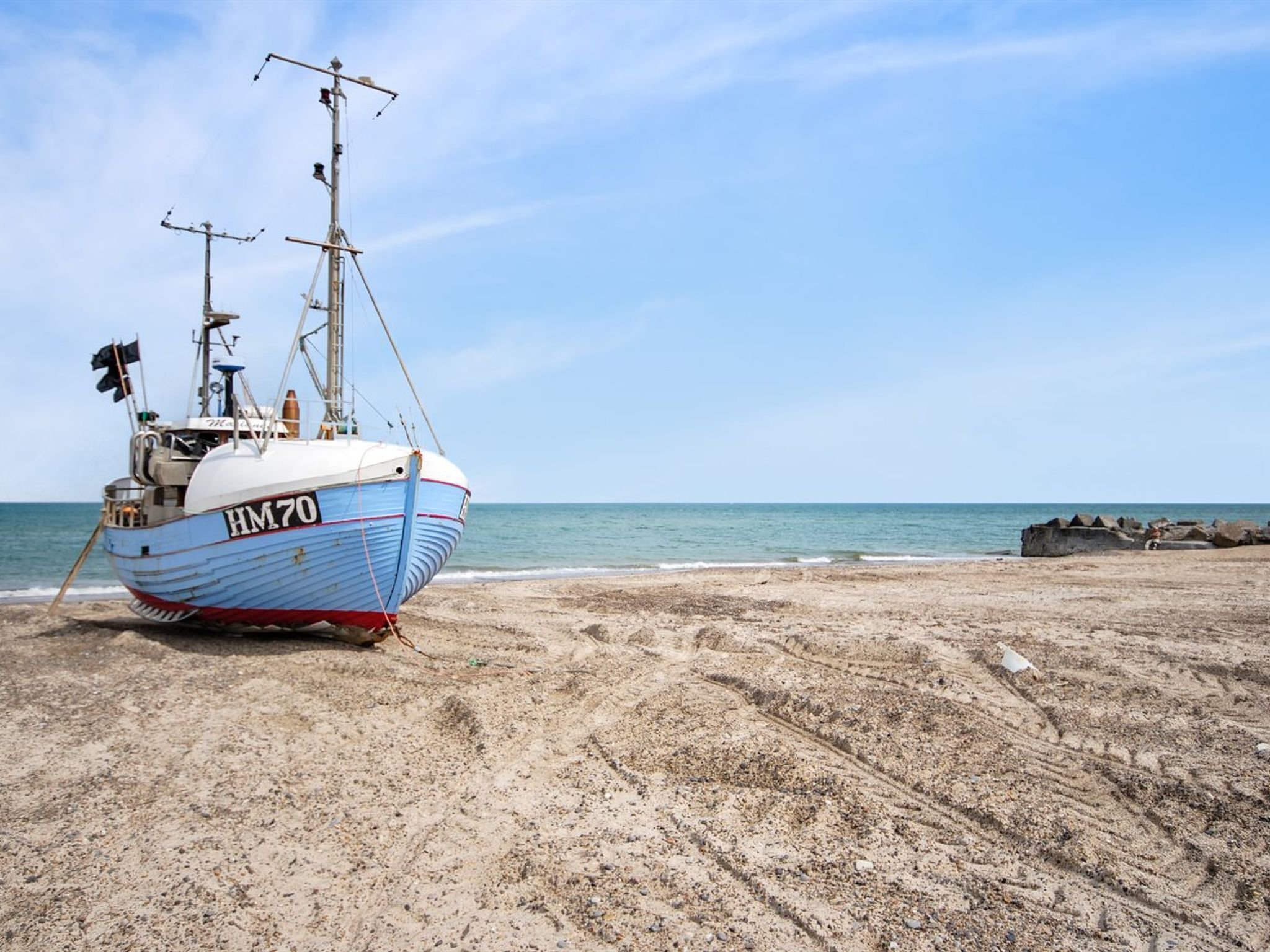A fishing boat with the registration HM70 on a sandy beach.