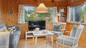 A cozy cabin interior with a wooden interior, a television, a bookshelf, and a window with curtains. - "Asmo" - 350m from the sea by Interhome (Fjerritslev)
