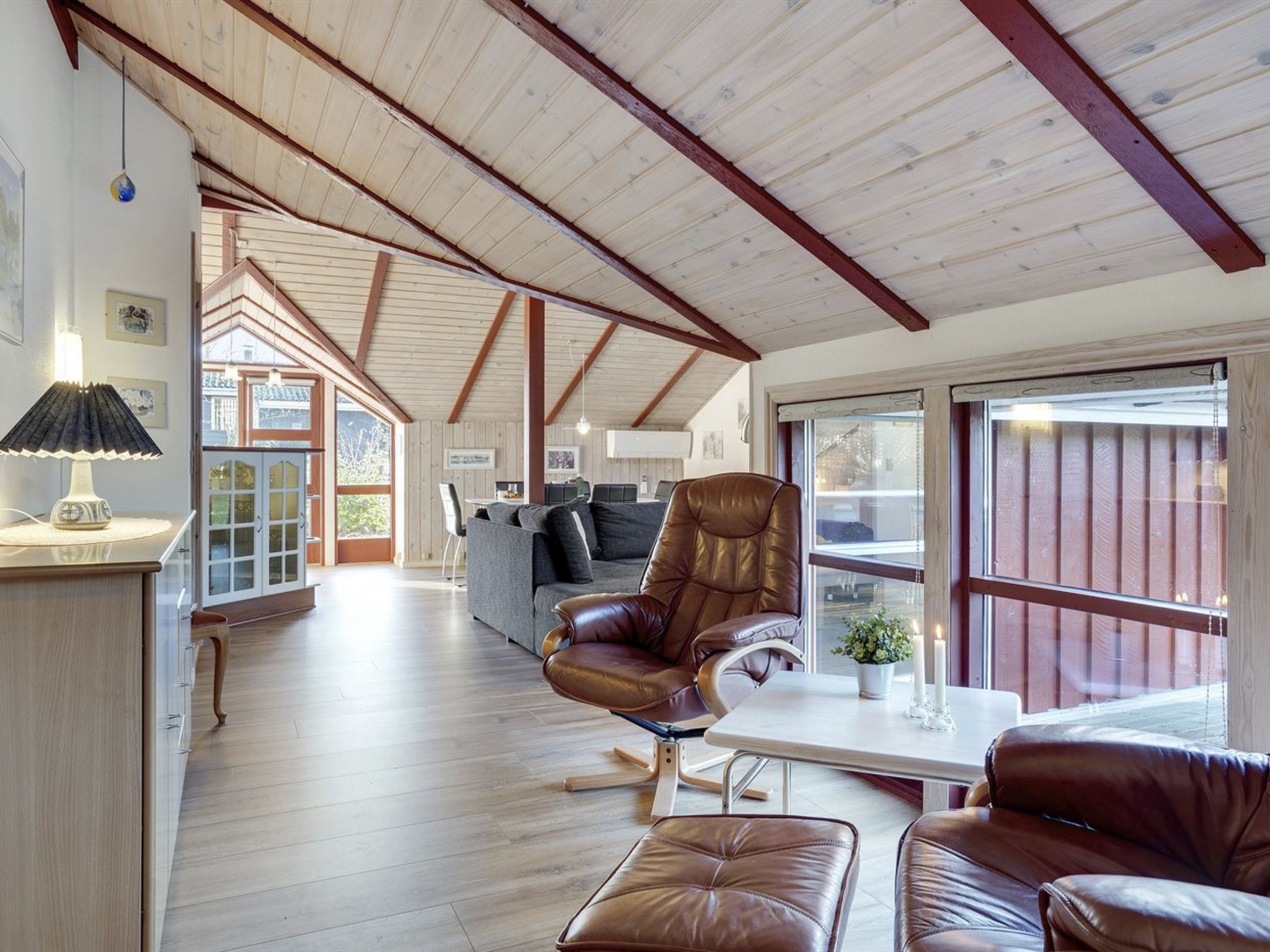 A spacious room with a high ceiling, wooden beams, a sofa, a leather armchair, and a dining table.