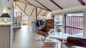Een ruime kamer met een hoge plafond, houten balken, een bank, een leren fauteuil en een eettafel.