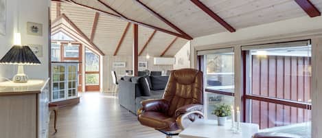 A spacious room with a high ceiling, wooden beams, a sofa, a leather armchair, and a dining table.