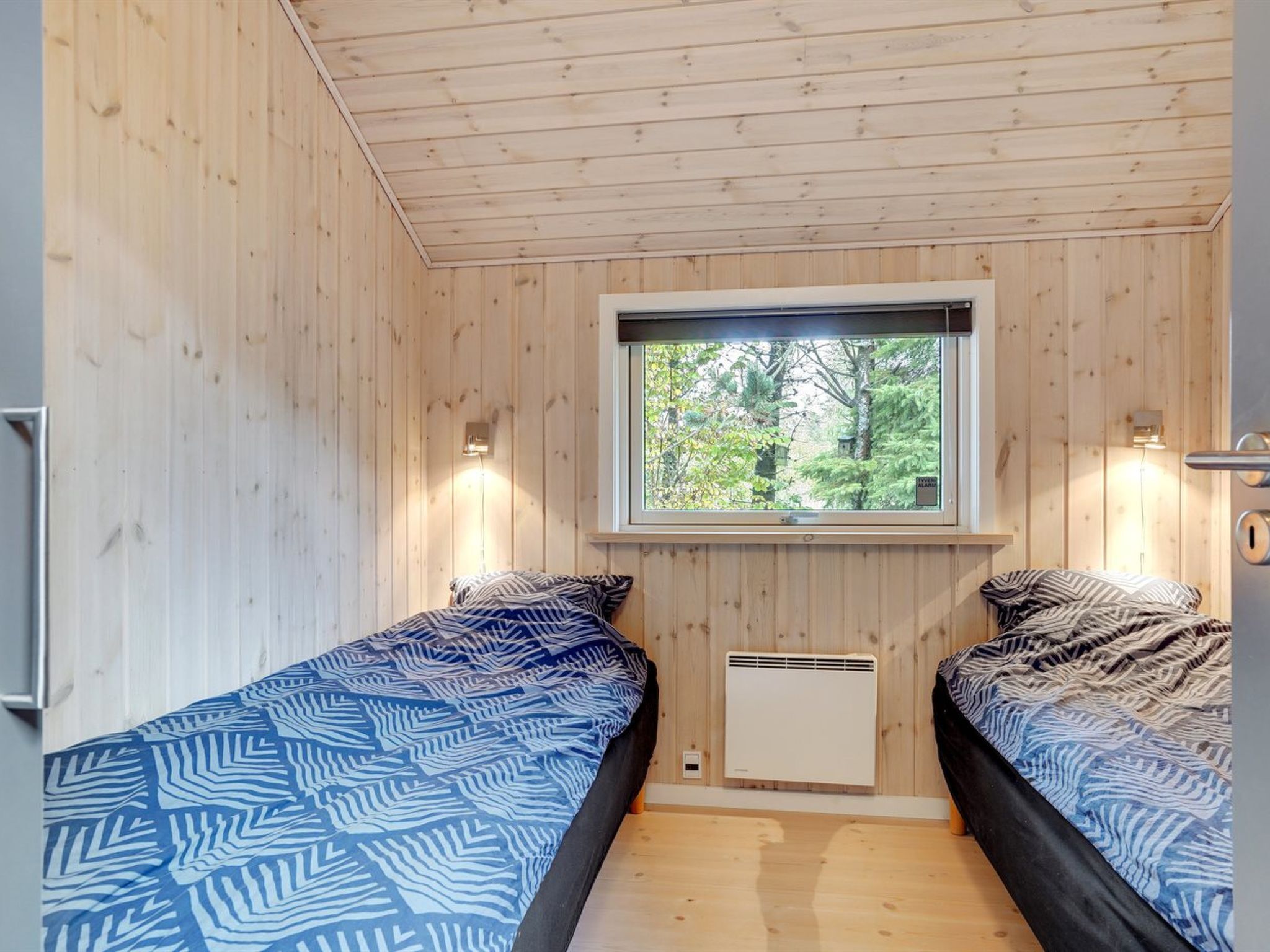 Een kamer met twee bedden, een raam met uitzicht op bomen en een klein, wit kastje.