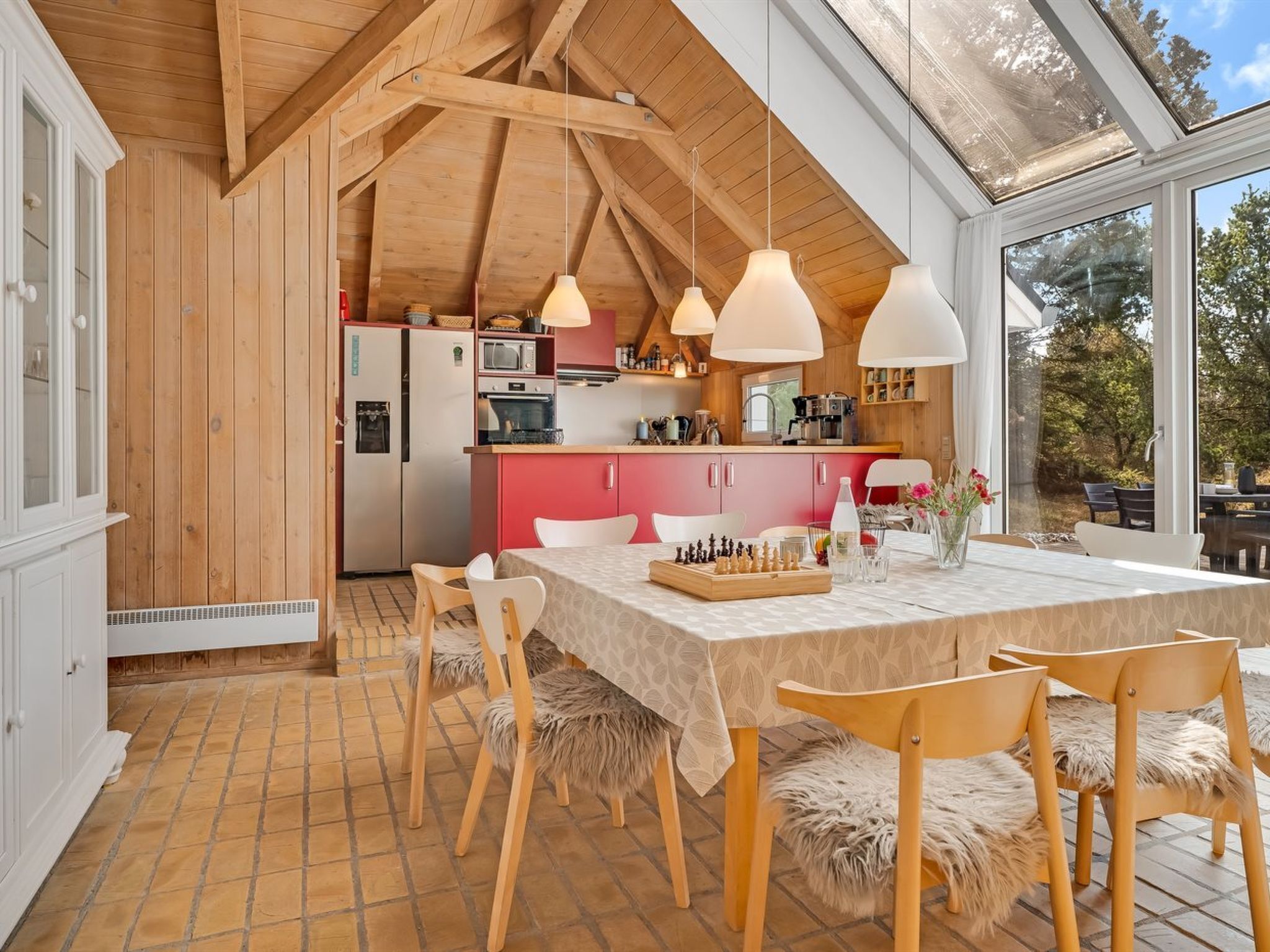 Une cuisine chaleureuse avec des poutres en bois, une table à manger avec des chaises et une vue sur l’extérieur.