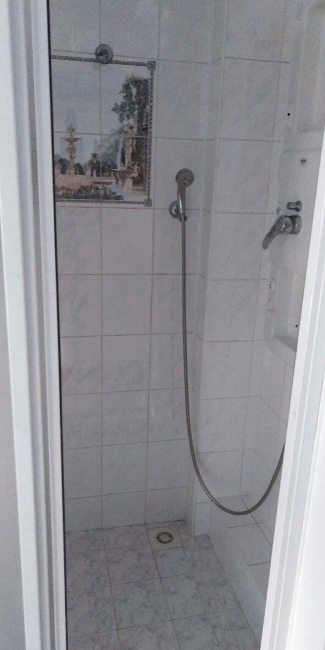 A small, tiled shower stall with a handheld showerhead and a wall-mounted faucet.