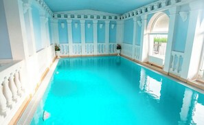En stor inomhuspool med vita kolonner och valv, omgiven av ljusblå väggar.