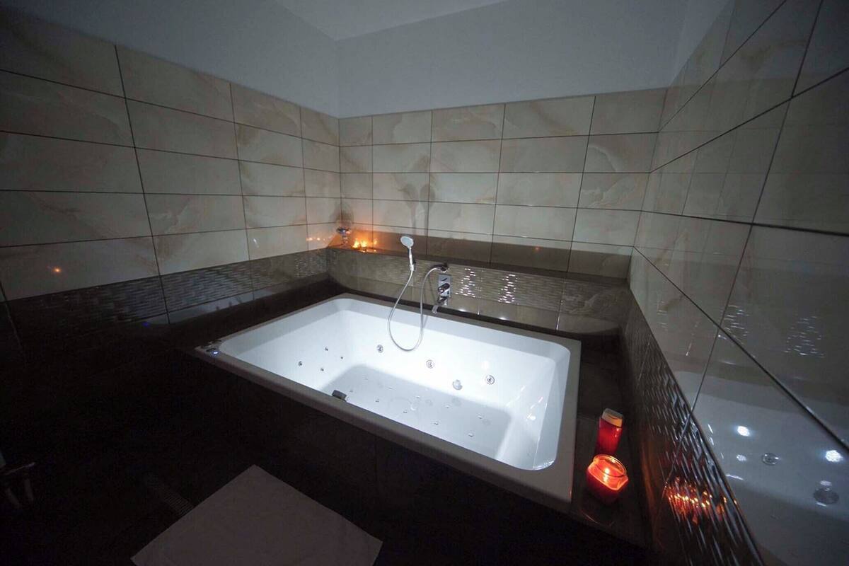 Un baño moderno con una bañera grande, paredes alicatadas y una vela pequeña a un lado.
